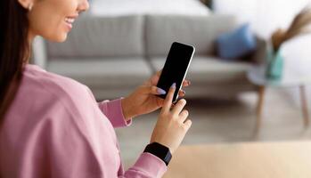 People And Technology Concept. Over The Shoulder View Of Positive Woman Using Smart Phone With Black Empty Screen For Mockup, Touching Device Display With Finger, Blurred Background, Selective Focus photo