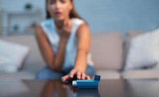 Unrecognizable Girl Reaching For Asthma Inhaler Preventing Attack Sitting On Sofa Indoor. Selective Focus, Shallow Depth photo