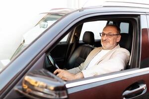 A mature man with glasses is contentedly seated in the driver seat of a stylish car, enjoying his drive in bright daylight, and displaying a relaxed demeanor. photo