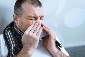 Sick Man Blowing Nose In Paper Tissue Having Fever Lying In Bed At Home During Coronavirus Epidemic Outbreak. Selective Focus photo