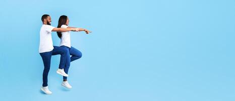 Full Body Length Of Excited Black Casual Couple Looking And Pointing With Fingers Aside At Copy Space On Blue Background, Man And Woman Walking And Demonstrating Free Place For Your Advert, Banner photo