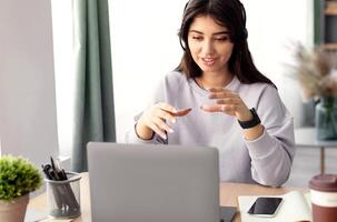 Online Call. Portrait of smiling woman sitting at desk, making virtual conference on laptop, talking and gesturing to webcam. Communication Concept. Female in headset chatting using computer photo