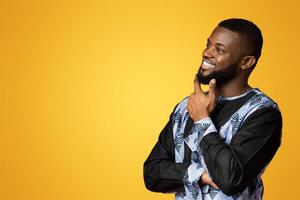 Thoughtful black man in traditional african costume staring at free space over pink studio background. Pensive african american guy looking at great offer, smiling and touching his chin, panorama photo