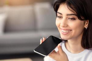 Closeup portrait of smiling young woman holding cellphone near mouth using mobile voice recognition or digital assistance app speaking with virtual assistant, recording message talking on smartphone photo