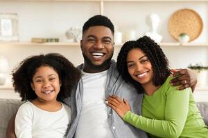 Happy African American Family Of Three Posing At Home, Sitting On Couch, Embracing And Smiling photo