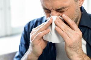 Coronavirus Concept. Sick Man Sneezing Blowing Nose In Paper Tissue Standing At Home During Covid-19 Pandemic Outbreak. Panorama, Selective Focus photo