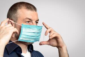 Man Putting On Protective Medical Mask For Virus Prevention Over Gray Background. Studio Shot photo