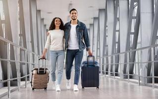 Ready For Vacation. Romantic Middle Eastern Couple Walking With Suitcases At Airport Terminal, Happy Arab Spouses Embracing While Going To Boarding Gate, Enjoying Travelling Together, Copy Space photo