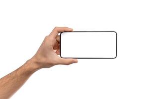 Man's hand holding modern smartphone with blank screen in horizontal orientation for mockup, copy space photo