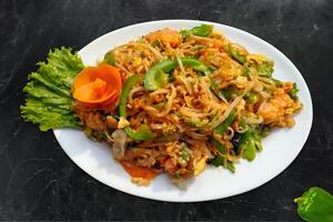 Chicken Chowmein. The dish consists of Chicken, Chinese Noodles, healthy vegetables, capsicum, lettuce, and carrot Served on a White Plate black background photo