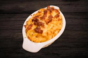 Macaroni filled with meat and mozzarella cheese in a white bowl on a wooden table photo