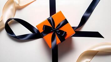 Top view of an orange gift box with black satin ribbon on cream surface. Minimalistic gift wrapping photo