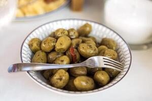 Green fragrant olives with spices. A close-up of a plate with delicious fruits of the olive tree and herbs on a white table. photo