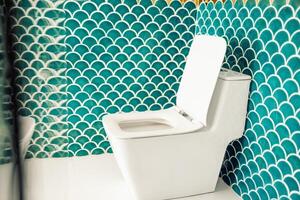 Close-up of a clean white toilet in a stylish bathroom. The modern neat room is decorated with contrasting blue and gold tiles in the form of fish scales. photo