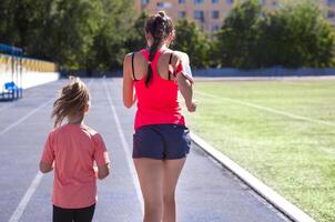Mother and little daughter are doing exercise in the stadium, back view photo