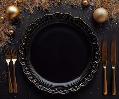 A black plate with a gold rim sits on a table with a fork, knife, and spoon photo