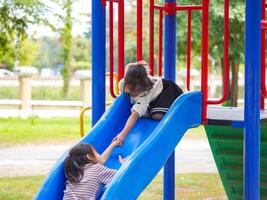 Cute sisters having fun on a colorful slide in an outdoor park. Children playing in the playground during summer vacation. photo