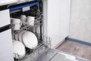 The door of the built-in dishwasher is open, close-up of plates and mugs photo