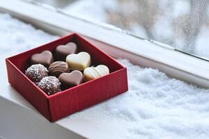 Heart shaped chocolates in a red velvet box by a snowy window, perfect for Valentine warmth photo