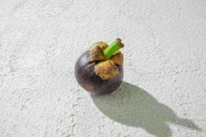 Mangosteen fruit displayed against a textured white background, emphasizing its unique purple rind and freshness photo