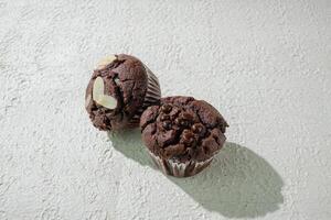 two chocolate muffins sitting on a white texture background photo
