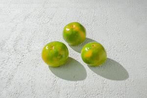 three green orange fruits on a white surface background photo