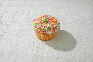 a cupcake with sprinkles on top of a white surface background photo