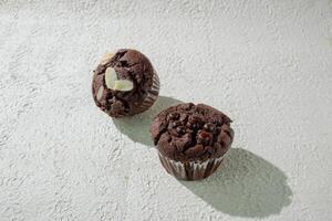 two chocolate muffins on a white surface background photo