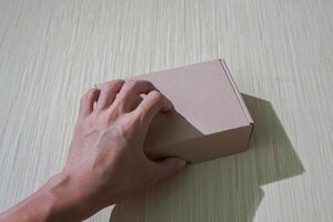 hand holding brown paper box isolated on a table, perfect for packaging or gifting, offering a simple mockup photo