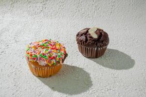 two cupcakes with sprinkles on top of a white surface photo