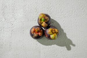 Mangosteen fruit displayed against a textured white background, emphasizing its unique purple rind and freshness. perfect for digital asset photo