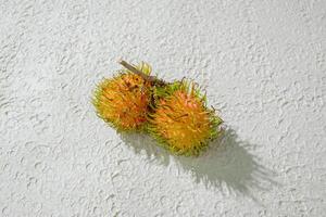 Fresh two yellow rambutan on a textured white background, perfect as a digital asset for design projects, posters, advertisements, or creative media photo