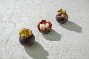 three different mangosteen fruits on a white surface photo