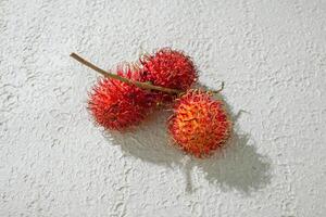 Fresh three red rambutan on a textured white background, perfect as a digital asset for design projects, posters, flyer, advertisements, or creative media photo