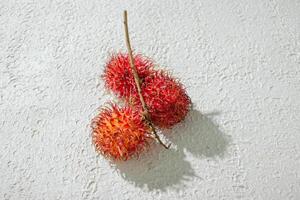 Fresh three red rambutan on a textured white background, perfect as a digital asset for design projects, posters, advertisements, or creative media photo