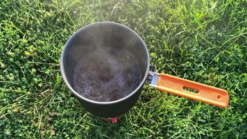 A closeup view of a pot filled with boiling water resting on lush green grass, with steam gracefully rising, perfect for themes related to outdoor cooking and camping adventures video