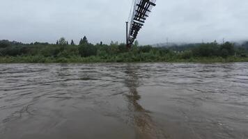 The highlights a flooded river, showcasing natures resilience and human engineering with a tall suspension bridge amid trees, reflecting both natures beauty and its challenges video