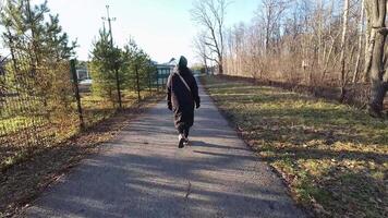 A solitary figure strolls down a paved path lined with lush trees, highlighting the tranquility of nature and the enjoyment of outdoor activities in a peaceful environment video