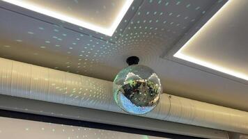 A contemporary disco ball lamp, designed to illuminate a modern interior space, is beautifully casting playful light patterns on the ceiling, creating a vibrant and lively ambiance video