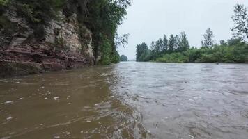 Experience the serene beauty of nature in this calming of a river flowing through a lush forest, with a stunning cliff backdrop. Watch the meandering river amid vibrant trees and rugged rocks video
