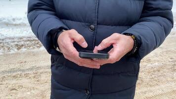A person in warm winter clothing uses a mobile phone in a snowy landscape, merging modern tech with nature, showcasing a balanced lifestyle and humanenvironment connection video