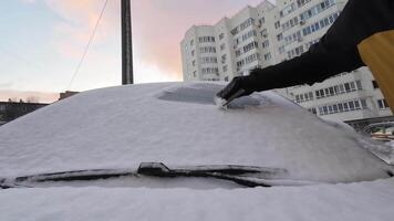 On a chilly winter morning, a person diligently brushes a thick layer of snow off their car windshield, while the surrounding residential buildings create a typical urban winter atmosphere video