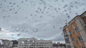 A captivating view through rainsoaked glass adorned with glistening droplets, showcasing gloomy buildings against a gray, overcast sky, which together create a moody urban atmosphere video