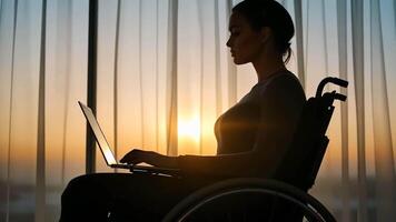 A silhouette of a Caucasian woman in a wheelchair using a laptop during sunset, symbolizing empowerment and accessibility, linked to International Day of Persons with Disabilities video
