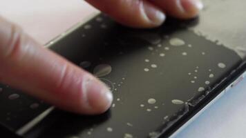 BARNAUL, SIBERIA, ALTAI REGION, RUSSIA - 15 June 2024. Finger interacting with water droplets on smartphone screen touch technology and hydrophobic coating in action. video