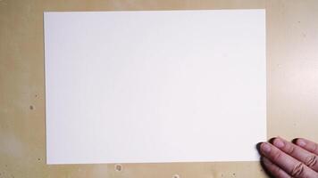 Caucasian male demonstrating paper placement technique on wooden surface for creative projects. video