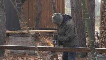 A man using a power tool creates sparks while working on a metal project in a forest setting during chilly weather, surrounded by trees and outdoor materials. video