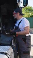 Senior vehicle mechanic with diagnostic tool laptop working near truck in workshop. Vertical video