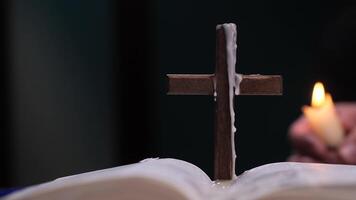 Wooden cross with candle wax drippings on open bible with lit candle in background video