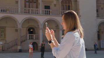 Frau mit Handy, Mobiltelefon Telefon zu nehmen Foto von historisch Gebäude im europäisch Stadt. weiblich Tourist erfasst Erinnerungen während Reise mit Smartphone video